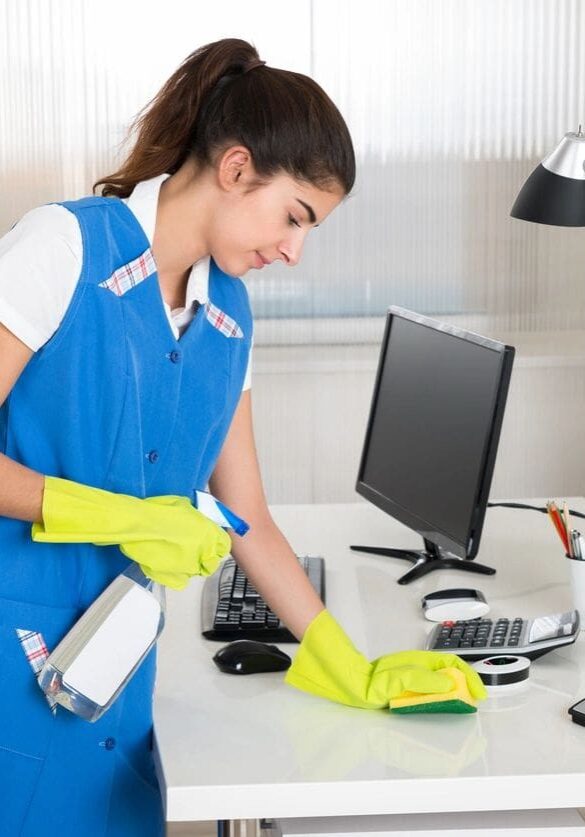 A woman in blue shirt cleaning desk with yellow gloves.