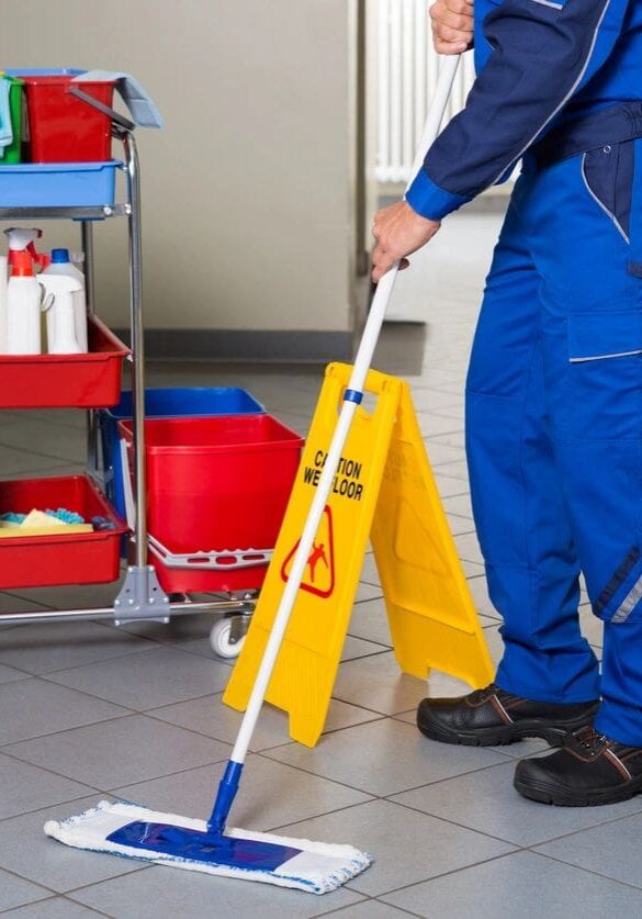 A man in blue overalls mopping the floor.